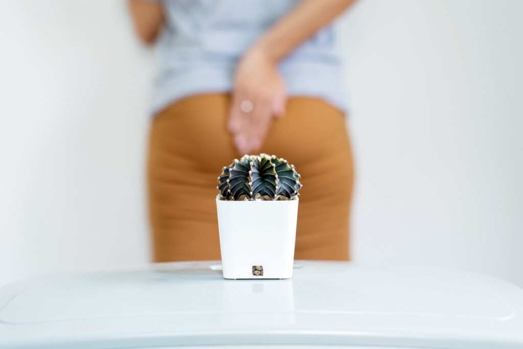 Blurred woman standing on white background with cactus and suffering from hemorrhoids